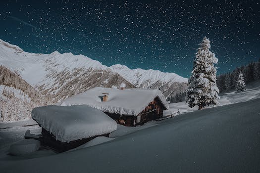 A serene winter night with cabins blanketed in snow, beneath an expansive starry sky and snow-capped mountains.